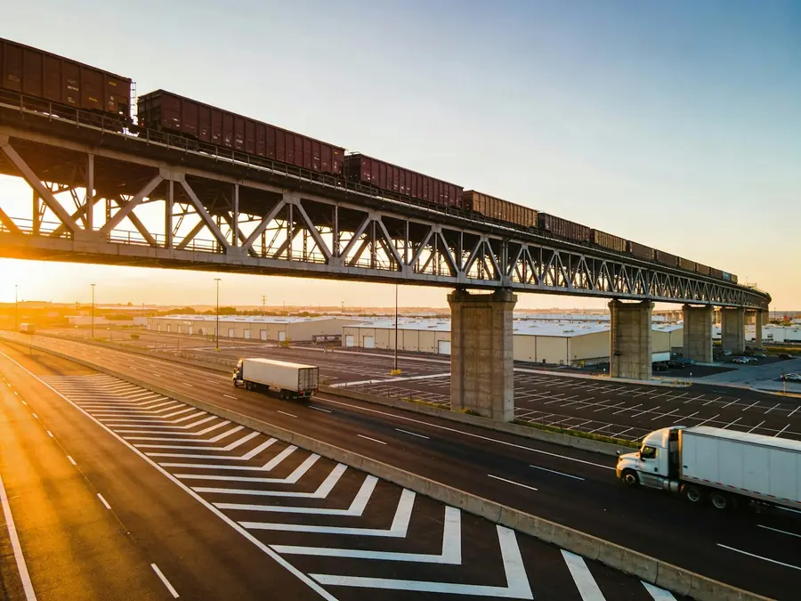 A freight train crosses an overpass above a highway at sunset